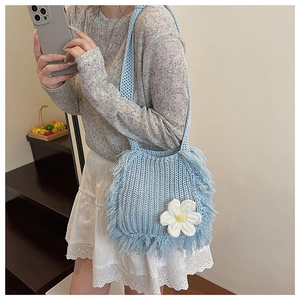 Detail of light blue handmade knit bag with white daisy decoration and tassel fringe