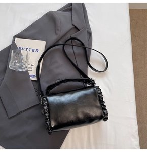 Detail of a black glossy leather tote bag with pleated edges and adjustable strap on a blazer