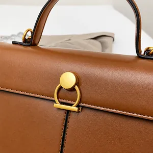 Detailed macro view of the gold circular buckle and stitching on the brown leather handbag