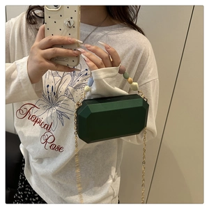 Detail of dark green geometric acrylic clutch bag with bead handle and gold chain