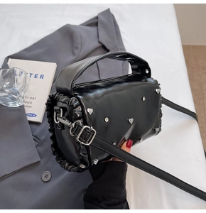 Detail of black glossy pillow bag featuring silver heart studs and ruched leather sides