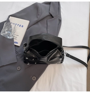 Detail of black glossy pillow bag with silver rivets and pleated side craftsmanship