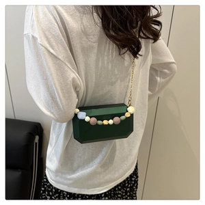 Macro shot of dark emerald geometric clutch with colorful bead handle and gold chain