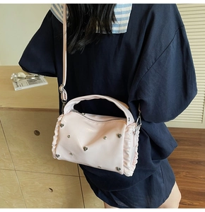 Pink glossy crossbody bag with heart studs and ruffled edges worn on a blue outfit
