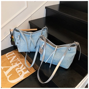 Dettaglio di strass scintillanti e targhetta M argento su borsa a mano in denim blu
