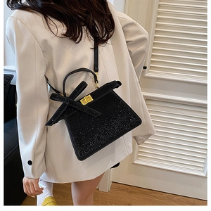 Détail du sac à main noir en strass avec fermoir doré et nœud chic en ruban de soie noir