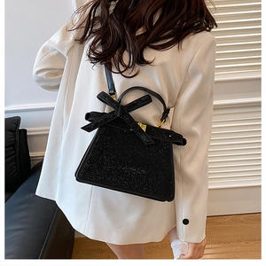 Détail d'un sac à main noir orné de strass brillants avec un nœud et une bandoulière chic