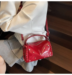 Detail of red glossy handbag with heart rivets and ruffle edges on wooden steps
