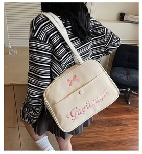 Detail of cream tote bag featuring pink bow embroidery and front magnetic pocket