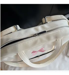 Detail of silver metal zipper closure and pink bow embroidery on white tote bag