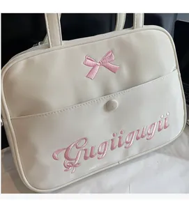 Detail of white tote bag featuring pink bow embroidery and front pocket with buckle