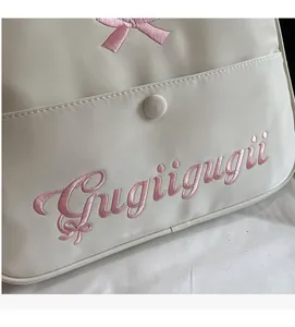Detailed macro view of cream leather tote bag featuring pink bow and text embroidery