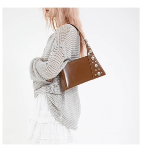 Brown leather shoulder bag with silver studs worn by a model in a minimal setting