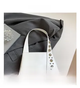Detailed close-up of white leather handbag with silver metal rivets on a grey fabric base