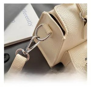 Detail shot of silver metal hook and strap attachment on beige lychee leather handbag