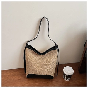 Detail of natural beige straw tote with black leather trim on a dark wooden surface