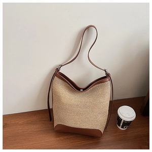 Detail of straw woven tote bag featuring premium brown leather trim and reinforced base