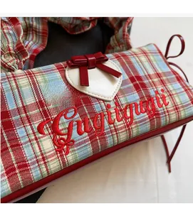 Detail of colorful plaid canvas tote featuring a white heart patch and red leather bow
