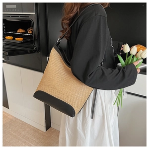 Detail of a large straw tote bag with black leather trim worn on the shoulder by a model
