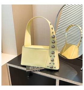 Detail of light yellow shoulder bag featuring silver stud hardware on wide strap
