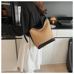 Straw shoulder tote bag with black leather stitching details in a modern kitchen setting