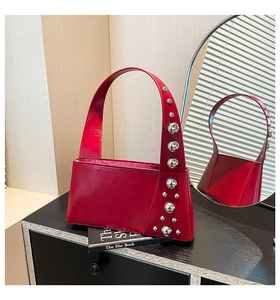 Detail of red glossy leather shoulder bag featuring decorative silver-tone metal rivets