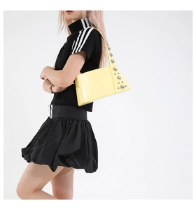 Detail of light yellow glossy shoulder bag featuring stylish silver metal rivets on strap