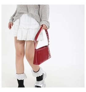 Detail of red patent leather shoulder bag with silver rivet studs on a studio model