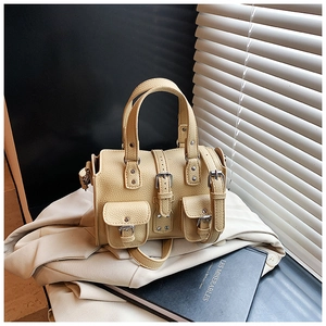 Detail view of beige lychee leather boston bag with metal buckles and front flap pockets