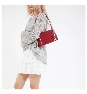 Detail of red patent leather shoulder bag with polished metallic rivets and glossy finish