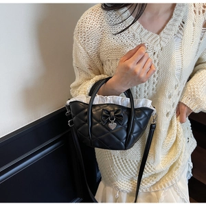 Close-up of black quilted bucket bag featuring a bow, heart pendant, and white lace lining