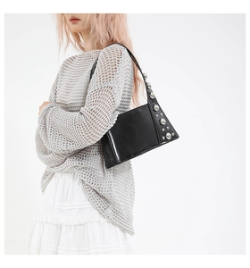 Detail of minimalist black leather underarm bag with silver stud accents on the strap