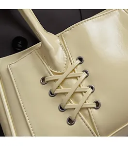 Détail de sac à main beige en cuir brillant avec laçage croisé et œillets métalliques