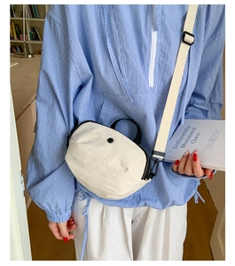 Gros plan du sac bandoulière en nylon léger blanc cassé avec sangle réglable porté par un modèle