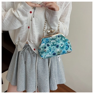 Detail of blue shell bag with floral 3D relief and elegant white pearl chain strap