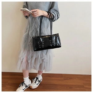 Détail du sac sous le bras en cuir verni noir avec laçage décoratif et œillets argentés