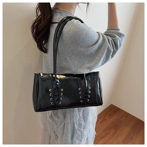 Détail du sac baguette noir brillant avec laçage latéral et œillets métalliques