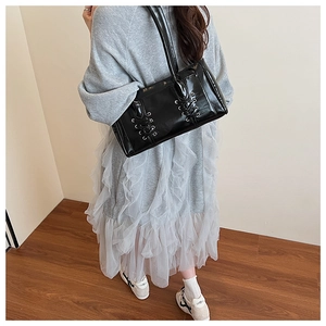 Détail du sac bandoulière en cuir verni noir avec rubans lacés et œillets métalliques