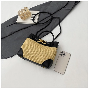 Close-up of woven straw handbag with black leather trim and golden metal knot buckle