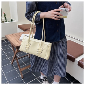 Sac bandoulière chic crème avec design à lacets croisés porté par un mannequin