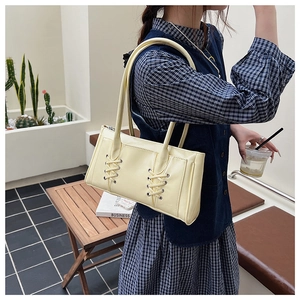 Détail d'un sac sous le bras jaune crème présentant un design à lacets croisés