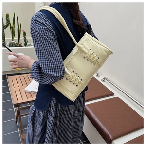 Détail d'un sac cabas en cuir jaune crème avec laçage croisé unique sur une terrasse