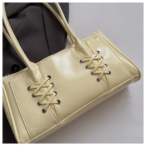 Détail du sac crème avec œillets lacés sur une surface en cuir lisse et brillant