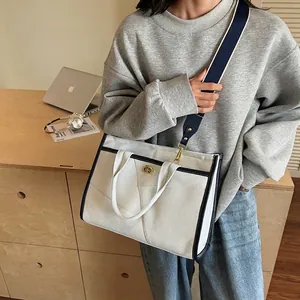 Grand sac cabas en toile beige avec bordure bleu marine et bandoulière sur un bureau