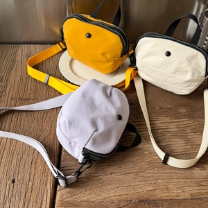 Trois sacs bandoulière minimalistes en nylon coloré posés sur une table en bois