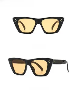 Detail view of black cat-eye sunglasses with yellow lenses and triple gold rivets