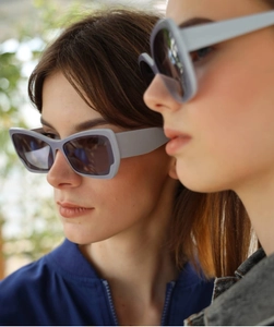 Detail of wide light grey butterfly sunglasses with dark lenses on female models