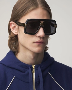 Detail of oversized square black sunglasses with gold metal trim and brand logo