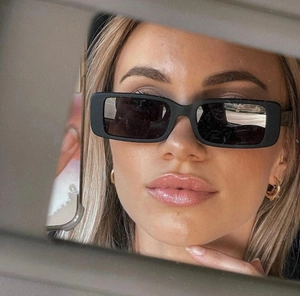 Close-up of black rectangular sunglasses with matte finish shown in a car mirror reflection