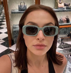 Detail view of sage green rectangular thick frame sunglasses worn in a fashion setting